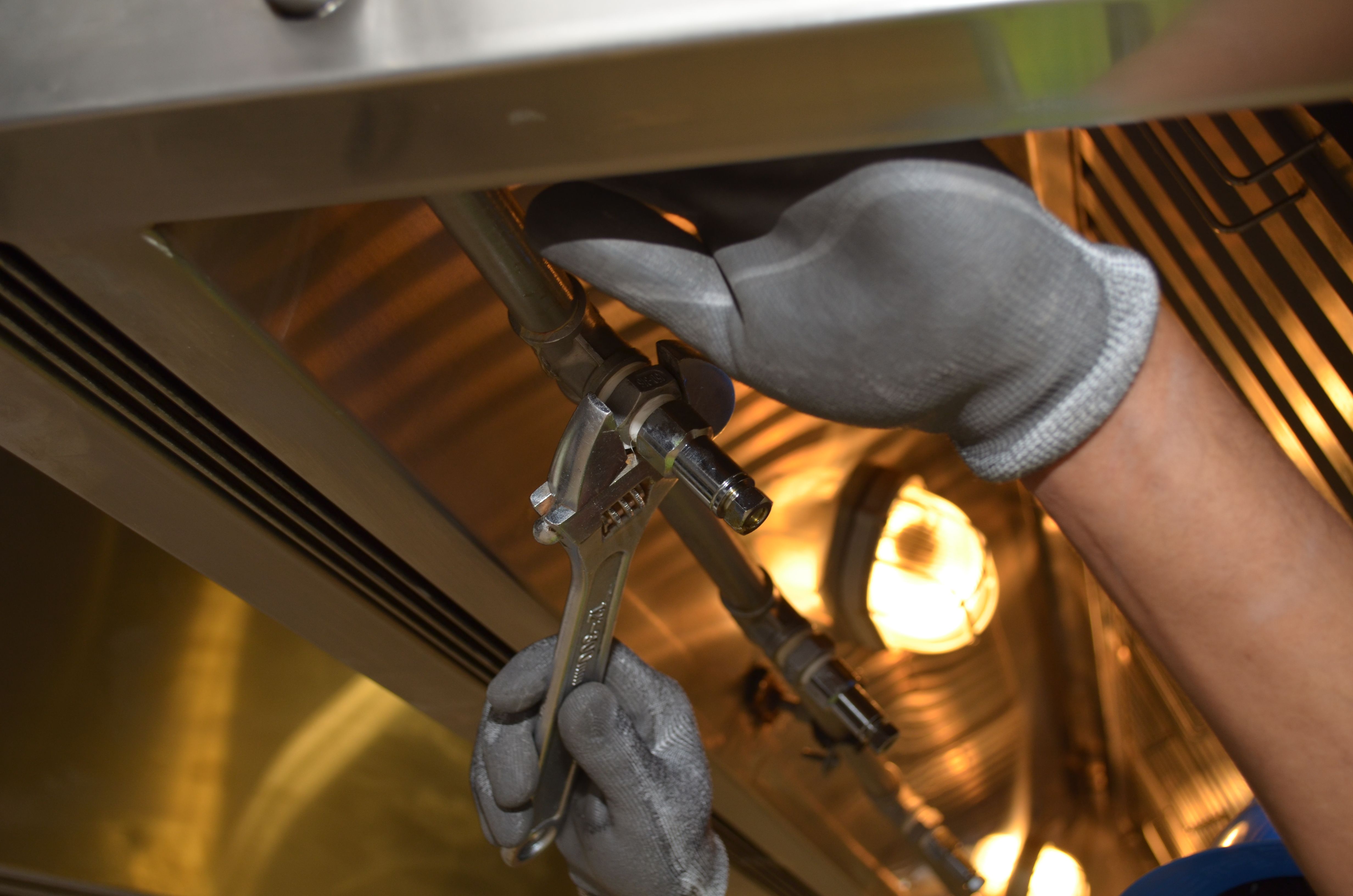 Gloved hand using a wrench to tighten a fitting under a sink