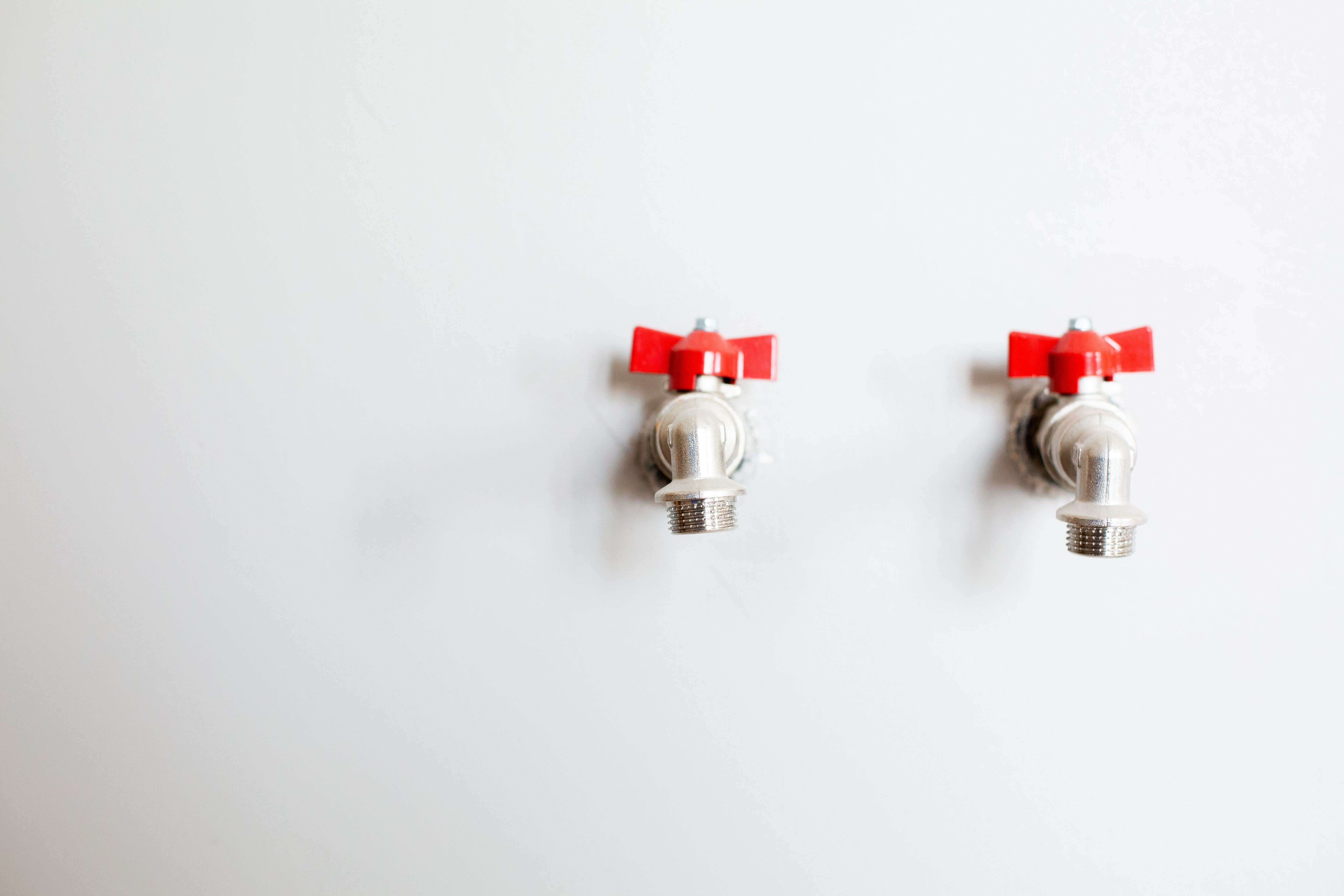 Two chrome shutoff valves with red handles mounted on a white wall