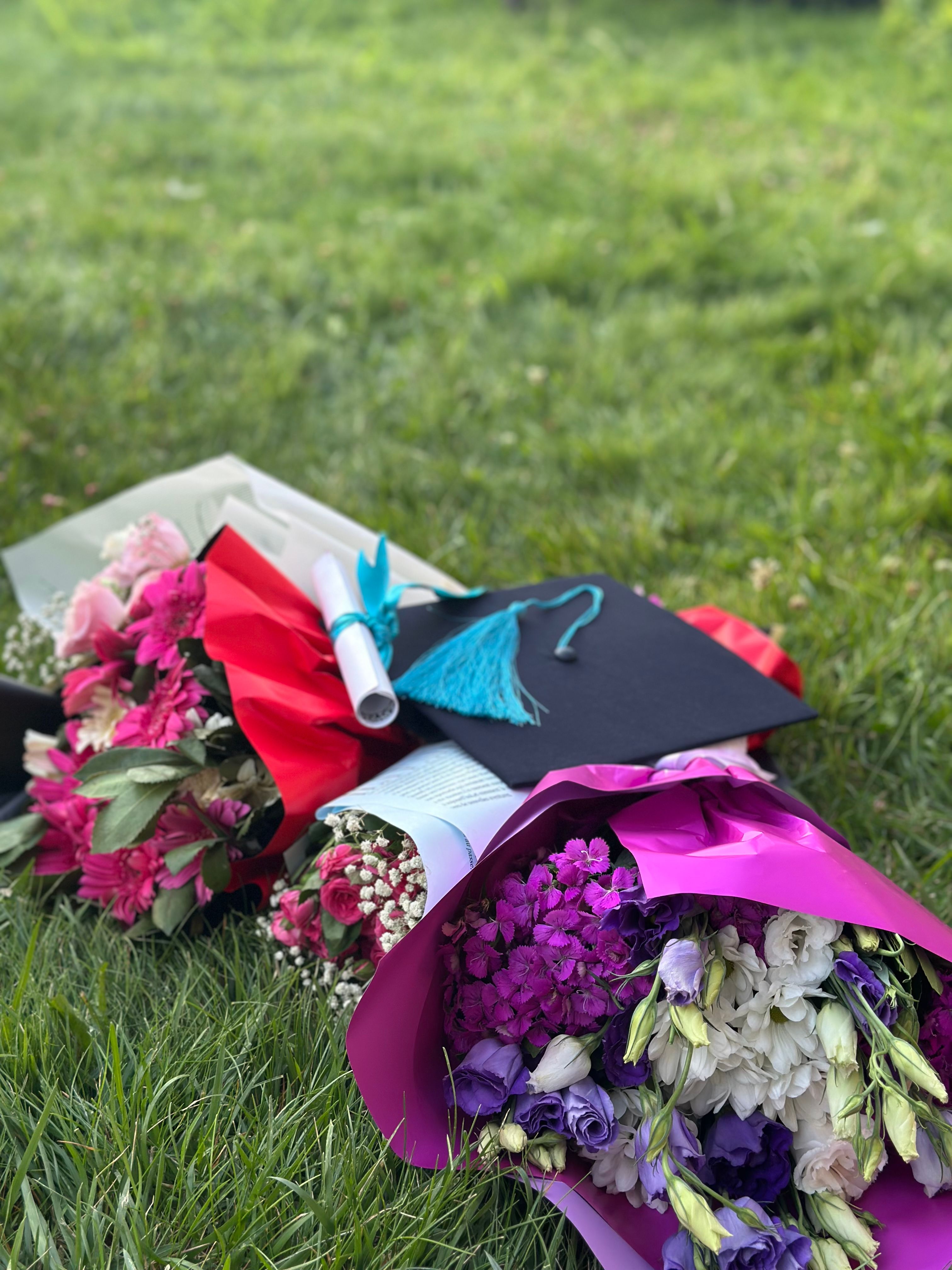 Wrapped bouquets resting on grass beside a graduation cap