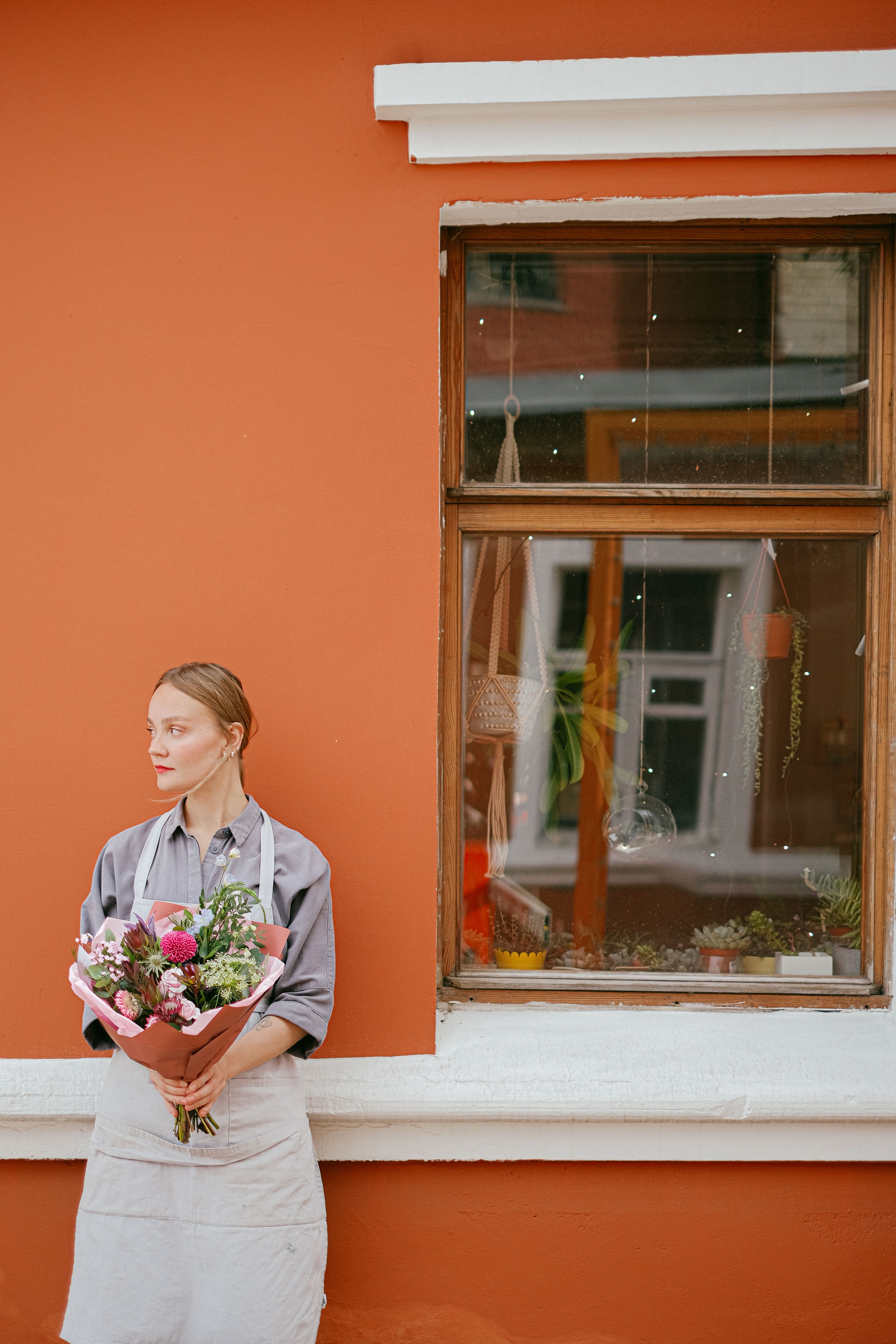 Florist in an apron holding a wrapped bouquet outside a shop